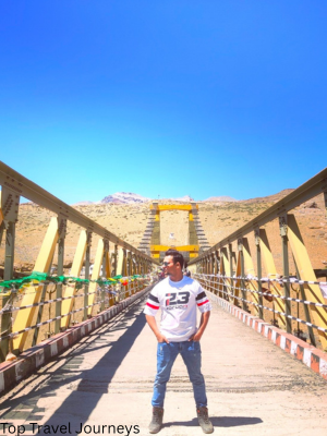 “Aamir Khan standing on Chicham Bridge in Spiti Valley with scenic mountains in the background”
