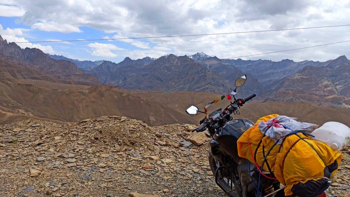 Fully loaded bike with jerry cans parked on a rugged road in Ladakh during a high-altitude journey