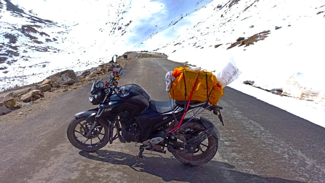 bike standing on a high-altitude road surrounded by snow-capped mountains on the route from Leh to Nubra Valley.